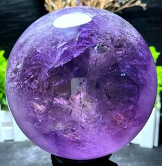 a large purple crystal ball sitting on top of a black table next to a potted plant