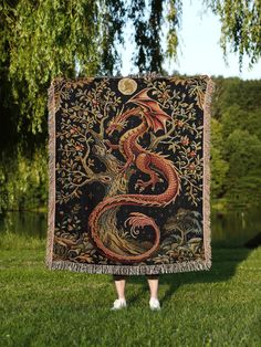 a woman standing in the grass holding up a tapestry