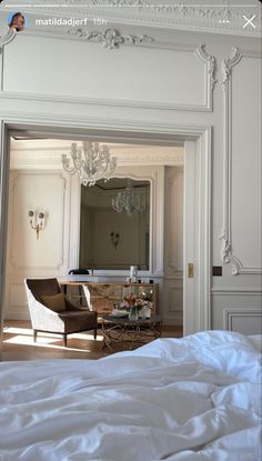 a white bed sitting in a bedroom next to a chandelier above a mirror