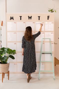 a woman writing on a wall next to a ladder and potted plant in front of it