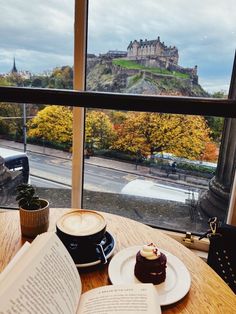 an open book sitting on top of a wooden table next to a cup of coffee