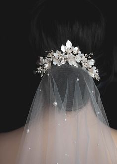 the back of a bride's head wearing a veil with flowers and pearls on it