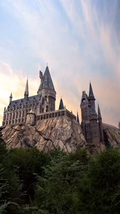 the hogwarts castle sits on top of a rock in front of some trees