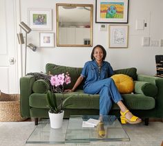 a woman sitting on top of a green couch next to a table with flowers in it