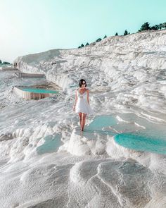 a woman in white dress standing on the edge of a body of water covered with ice