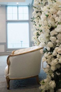 a white chair sitting next to a tall flower covered tree in an empty room with large windows