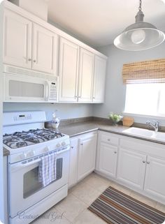 a kitchen with white cabinets and an oven in the corner, along with a striped rug on the floor