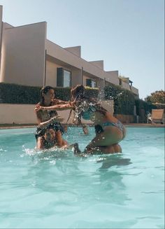 four girls are playing in the pool with their arms around each other and splashing water