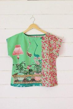 a green shirt with pink flowers and birds on it hanging from a wooden hanger