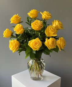 a vase filled with yellow roses sitting on top of a white table next to a gray wall