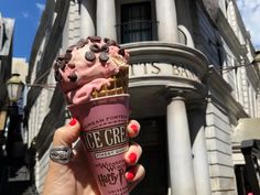 a person holding up an ice cream cone with chocolate chips on it in front of a building