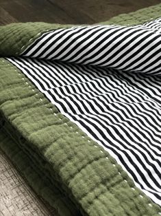 a green and black quilted blanket laying on top of a wooden floor next to a pillow