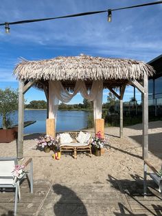 a gazebo with flowers on the ground next to some chairs and a body of water