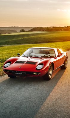 a red sports car parked on the side of a road in front of a grassy field