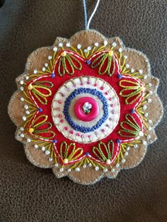 an ornament made out of fabric and thread with a pink button in the center