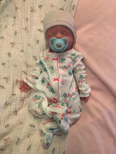 a baby wearing a pacifier laying on top of a bed next to a pillow