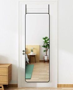 a mirror reflecting a room with a potted plant on the floor and a table