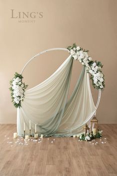 a wedding arch decorated with white flowers and greenery on the floor next to candles