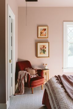 a bedroom with pink walls and pictures hanging on the wall above the bed, along with a red chair