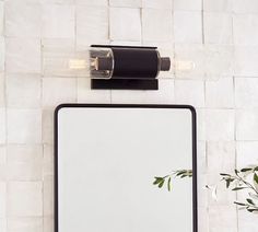 a bathroom mirror with a light on it next to a plant