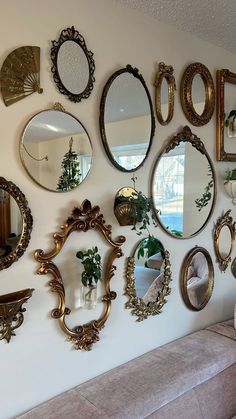 there are many mirrors hanging on the wall next to a couch and table with flowers in vases