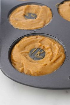 four cupcakes in a muffin tin with peanut butter on top, ready to go into the oven