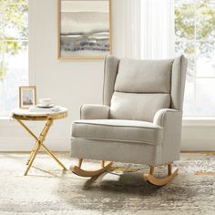 a rocking chair in front of a window with a tray on the floor next to it