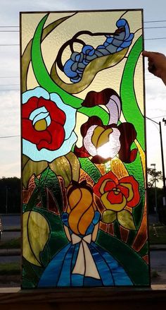 a stained glass window with flowers and vines on it, being held up by a hand