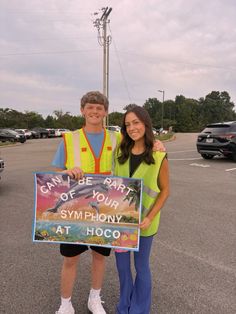 two people standing in a parking lot holding a sign