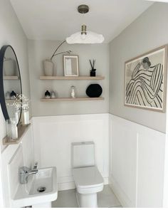 a white toilet sitting in a bathroom next to a sink under a framed art piece