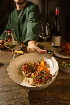 a man sitting at a table in front of a plate of food and wine glasses