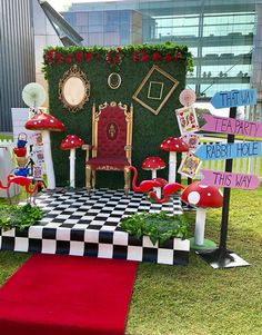 an outdoor stage set up for a party with red chairs and green plants on it