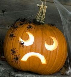 a carved pumpkin with faces on it and spider webs around the face, in front of a stone wall