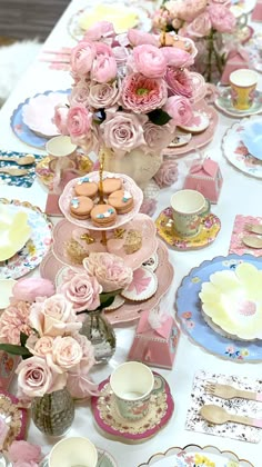 a table topped with plates and cups filled with pink flowers next to each other on top of a white table cloth