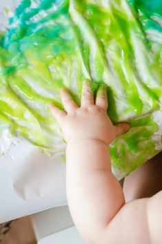 a baby is playing with some green and white dye on the paper it's made