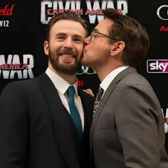 two men in suits kissing each other on the red carpet