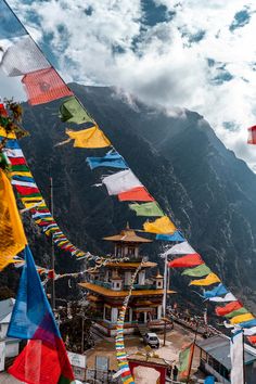 there are many colorful flags flying in the air near a mountain side town with mountains behind it