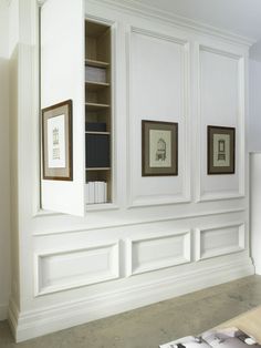 an empty room with white paneling and framed pictures on the wall, along with bookshelves