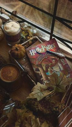 an assortment of food and drink items on a table near a window with autumn leaves