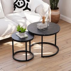 two tables sitting on top of a wooden floor next to a white couch and potted plant