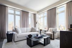 a living room filled with white furniture and large window covered in drapes, overlooking the city