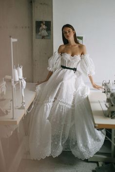 a woman in a white dress standing next to a sewing machine