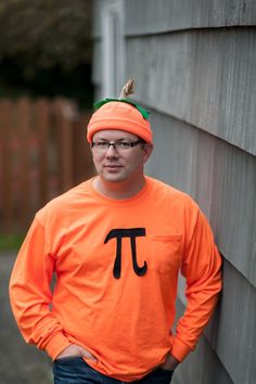 a man in an orange shirt with a pi on it's chest standing next to a wall