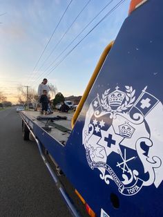 a man riding on the back of a blue truck down a street next to another person