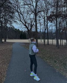 a woman standing on a path in the middle of a park with trees around her