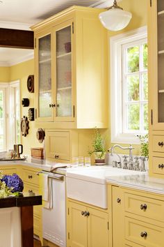 a kitchen with yellow cabinets and white counter tops is pictured in this image, there are two windows above the sink