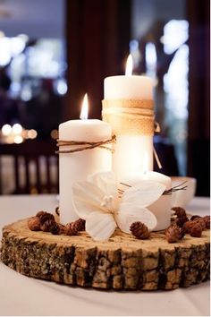 two white candles sitting on top of a piece of wood