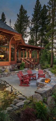 a fire pit surrounded by red chairs and tables in front of a log cabin style home