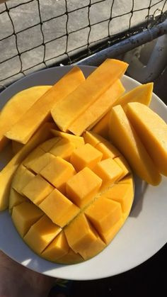 a white plate topped with sliced mangoes on top of a wooden table next to a net