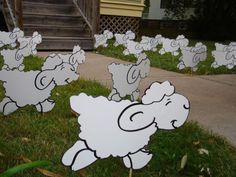 several sheep cut out in the grass near a house and yard with lawn mowers